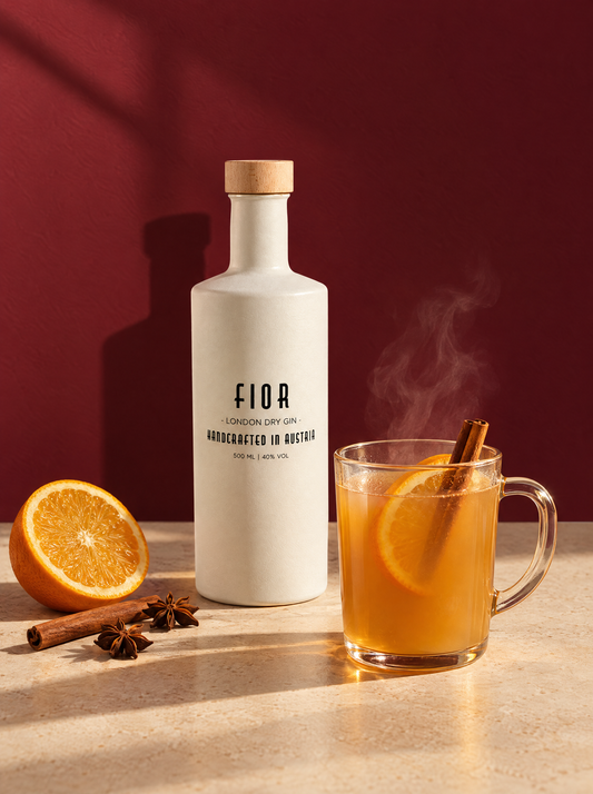 FIOR Glüh-Gin im Glas mit Zimtstange und Orange neben der Gin FIOR Flasche